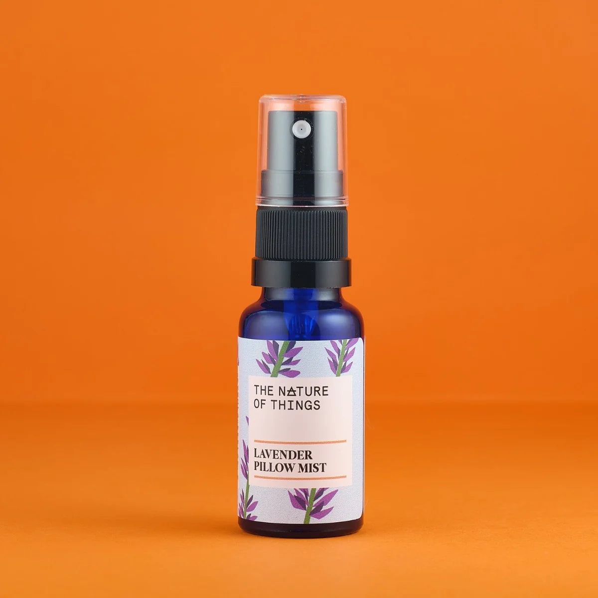 Blaue 20ml-Sprühflasche mit schwarzem Pumpkopf und einem Etikett mit der Aufschrift „The Nature of Things Lavender Pillow Mist“ vor orangefarbenem Hintergrund.
