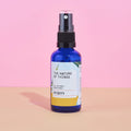 Blaue 50ml-Sprühflasche des Purity Room Sprays von The Nature of Things mit gelb-weißem Etikett und schwarzem Sprühkopf vor rosa-beigem Hintergrund.
