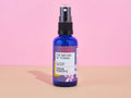 Blaue Glasflasche des Think Positive Room Sprays von The Nature of Things vor rosa-beigem Hintergrund.