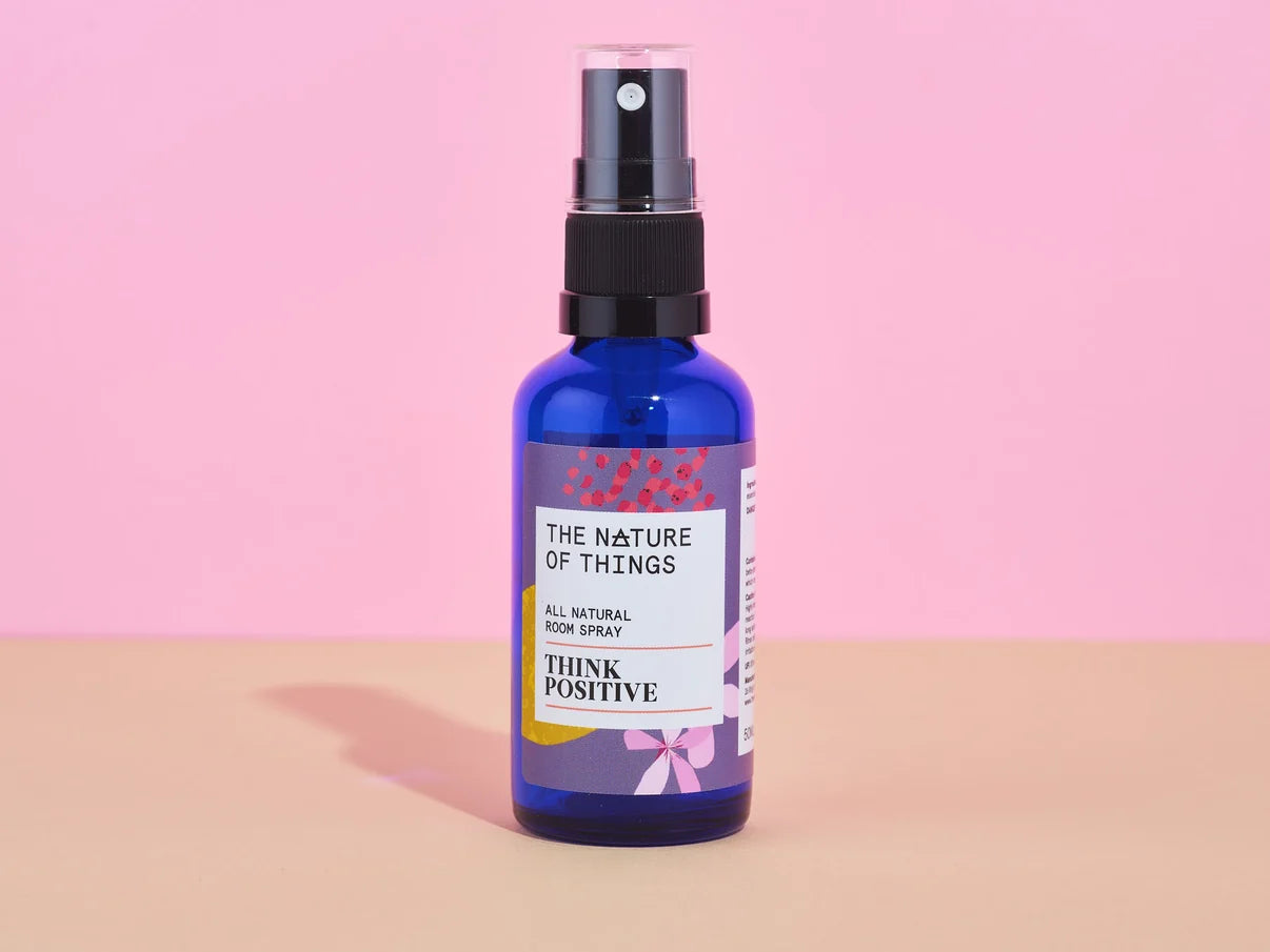 Blaue Glasflasche des Think Positive Room Sprays von The Nature of Things vor rosa-beigem Hintergrund.