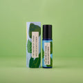 Blauer 10-ml-Roll-On und dazugehörige hellblaue Umverpackung mit grünen Blatt-Illustrationen vor einem grünen Hintergrund.