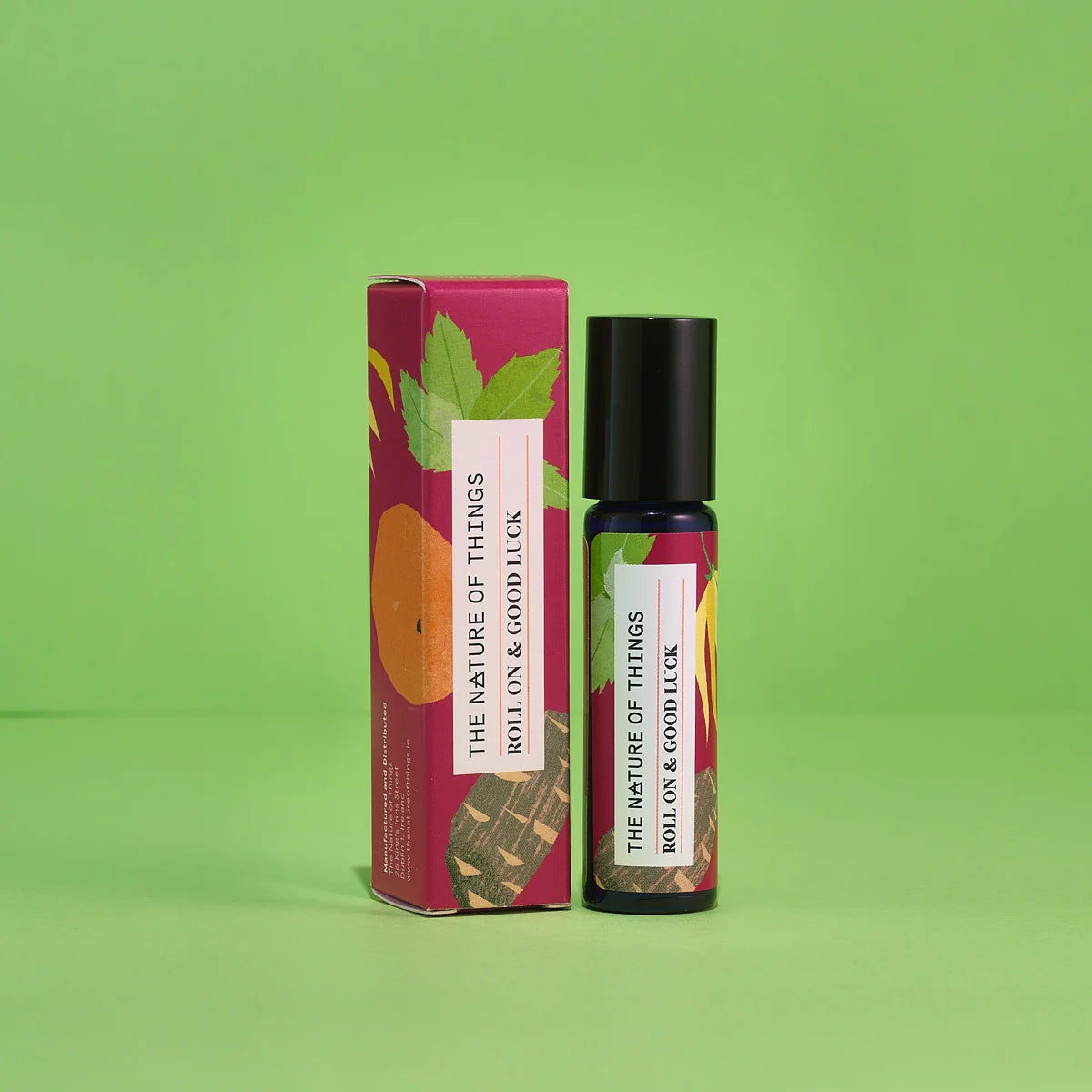 Blauer 10-ml-Roll-On und dazugehörige pinke Umverpackung mit Orangen- und Blatt-Illustrationen vor einem grünen Hintergrund.