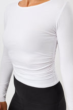 Blonde Frau von vorne in einem weißen Langarmshirt "Side Ruffled" mit Rundhalsausschnitt und seitlichen Raffungen vor hellem Hintergrund.