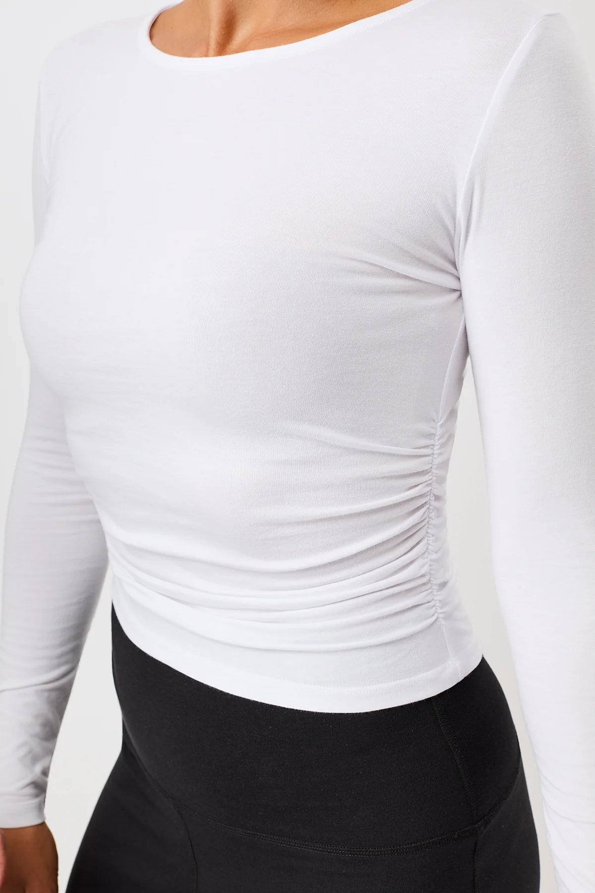 Blonde Frau von vorne in einem weißen Langarmshirt "Side Ruffled" mit Rundhalsausschnitt und seitlichen Raffungen vor hellem Hintergrund.
