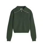 Dunkelgrüner Pullover "Tanit" von Thinking Mu aus Merinowolle mit hohem Kragen, silbernem Reißverschluss und Label am Ausschnitt vor hellem Hintergrund.