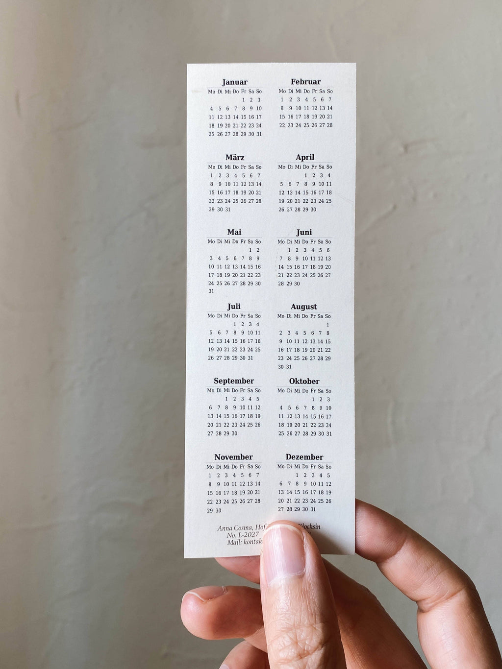 Ein Lesezeichen von Anna Cosma mit rosagelbem Farbverlauf und goldfoliiertem Aufdruck „2027 You are here to shine“ sowie Kalenderübersicht auf der Rückseite.