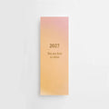 Ein Lesezeichen von Anna Cosma mit rosagelbem Farbverlauf und goldfoliiertem Aufdruck „2027 You are here to shine“ sowie Kalenderübersicht auf der Rückseite. koblenz
