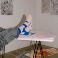 Ein Paar blaue Socken mit beigen und violetten, abstrakten Farb- und Blockmustern sowie beiger Fersen- und Zehenpartie vor hellem Hintergrund.