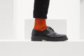 Ein Paar gestrickte Socken aus Wolle in meliertem Rostorange vor weißem Hintergrund.