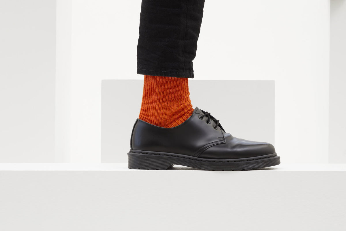 Ein Paar gestrickte Socken aus Wolle in meliertem Rostorange vor weißem Hintergrund.