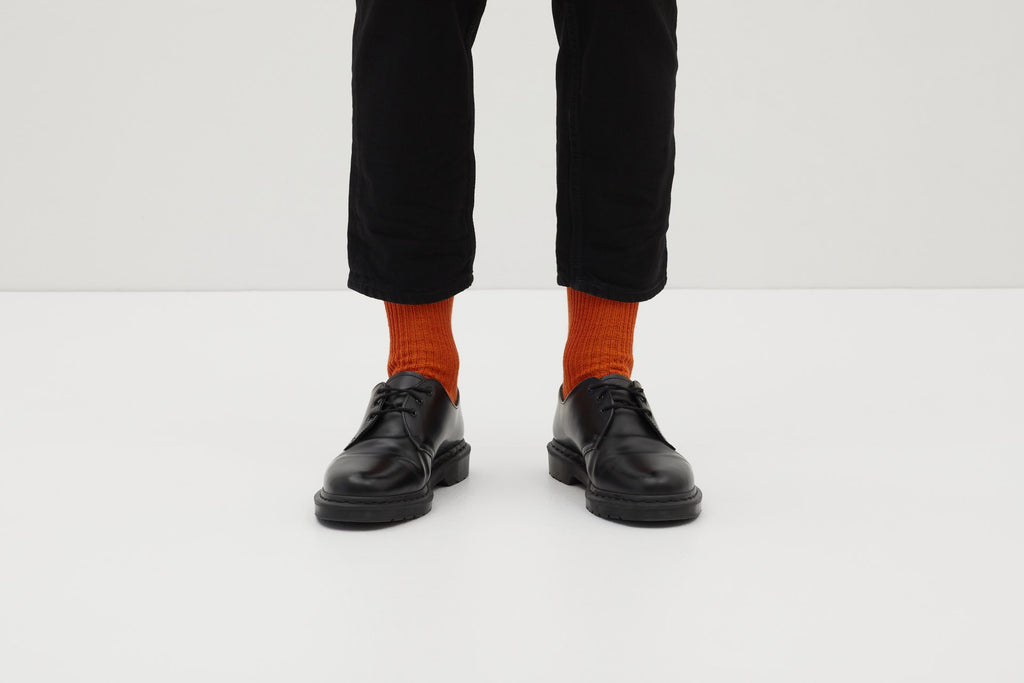 Ein Paar gestrickte Socken aus Wolle in meliertem Rostorange vor weißem Hintergrund.
