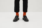 Ein Paar gestrickte Socken aus Wolle in meliertem Rostorange vor weißem Hintergrund.