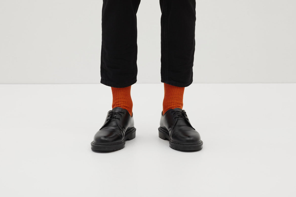 Ein Paar gestrickte Socken aus Wolle in meliertem Rostorange vor weißem Hintergrund.