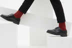 Ein Paar gestrickte Socken aus Wolle in meliertem Rot vor weißem Hintergrund.