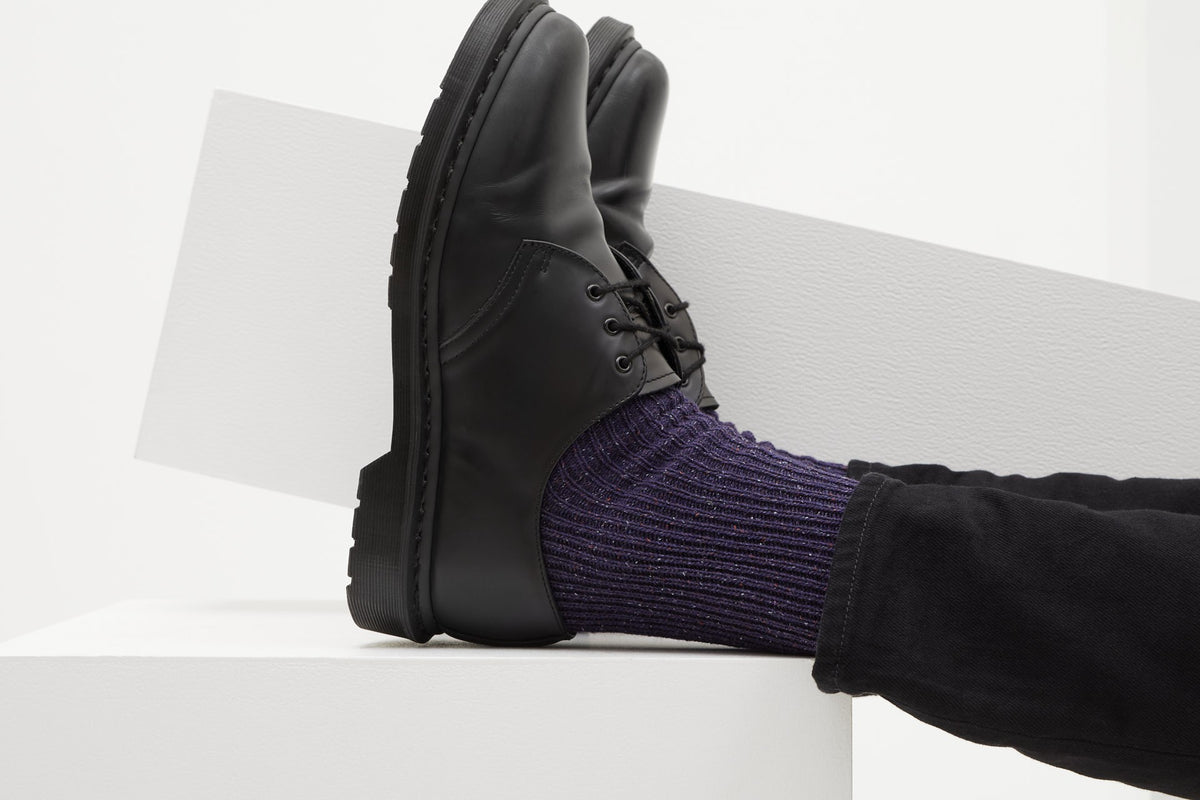 Ein Paar gestrickte Socken aus Wolle in meliertem Violett vor weißem Hintergrund.