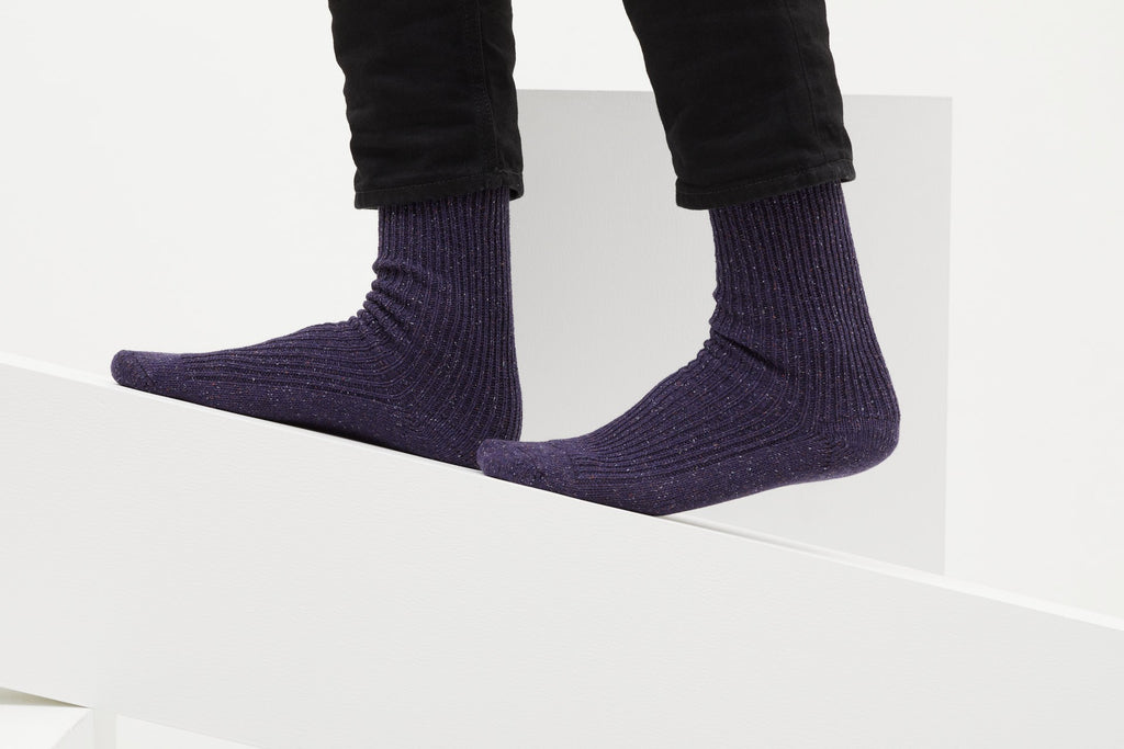Ein Paar gestrickte Socken aus Wolle in meliertem Violett vor weißem Hintergrund. seide