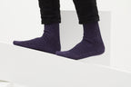Ein Paar gestrickte Socken aus Wolle in meliertem Violett vor weißem Hintergrund. seide