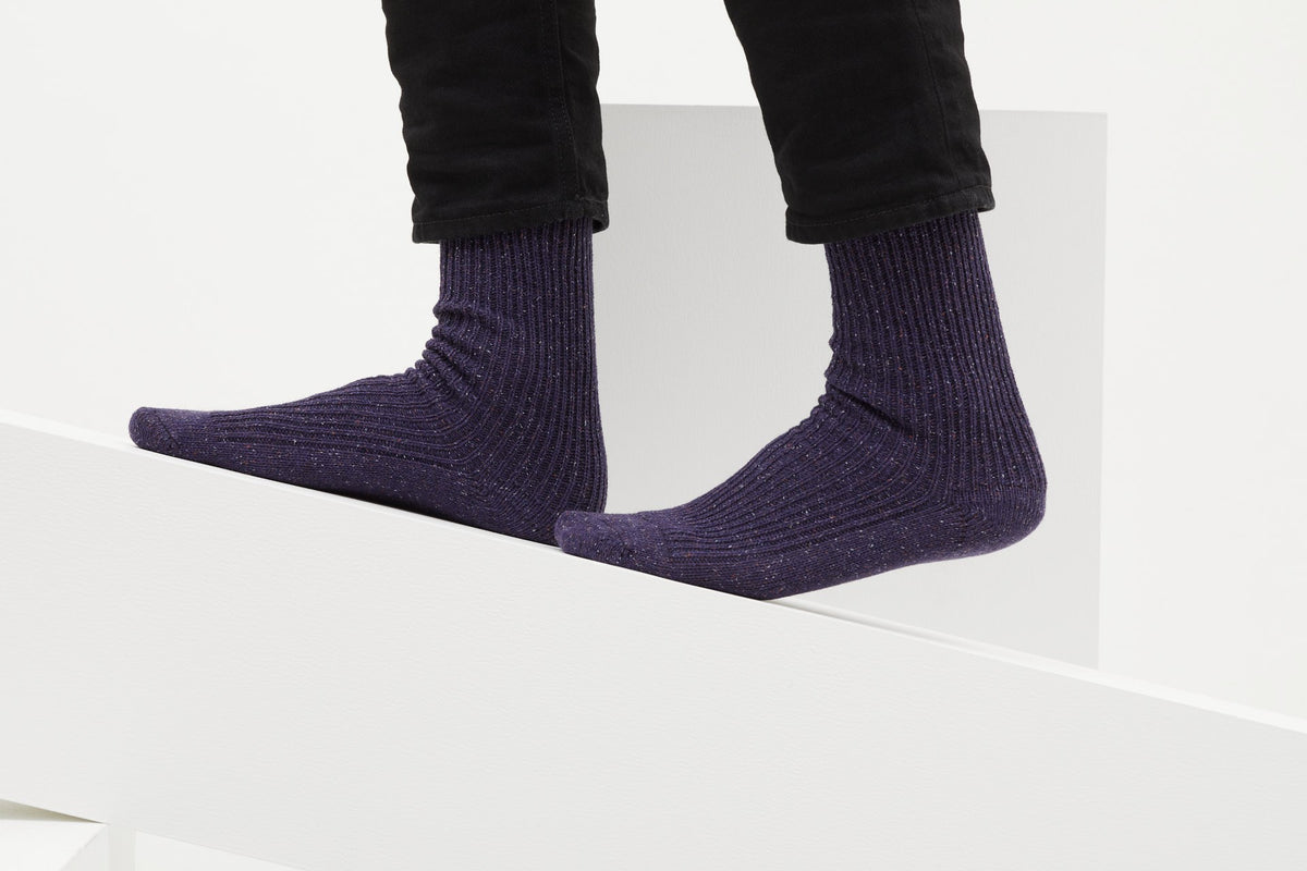 Ein Paar gestrickte Socken aus Wolle in meliertem Violett vor weißem Hintergrund. seide