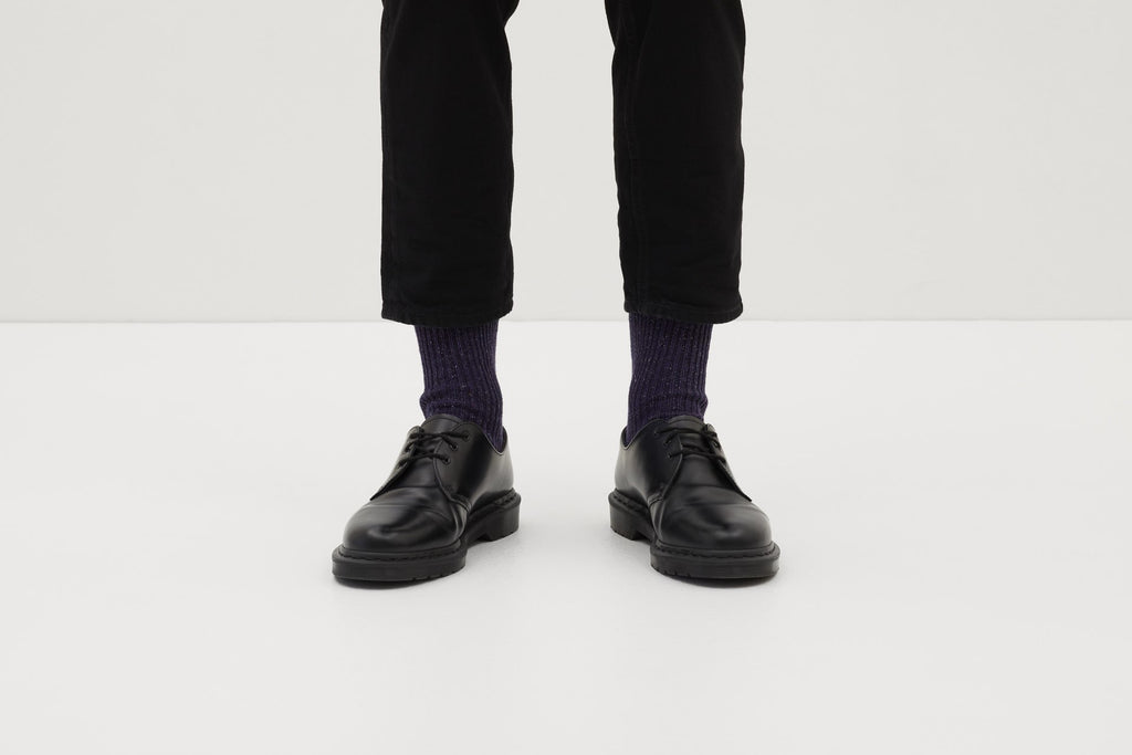Ein Paar gestrickte Socken aus Wolle in meliertem Violett vor weißem Hintergrund. seide ferdinand