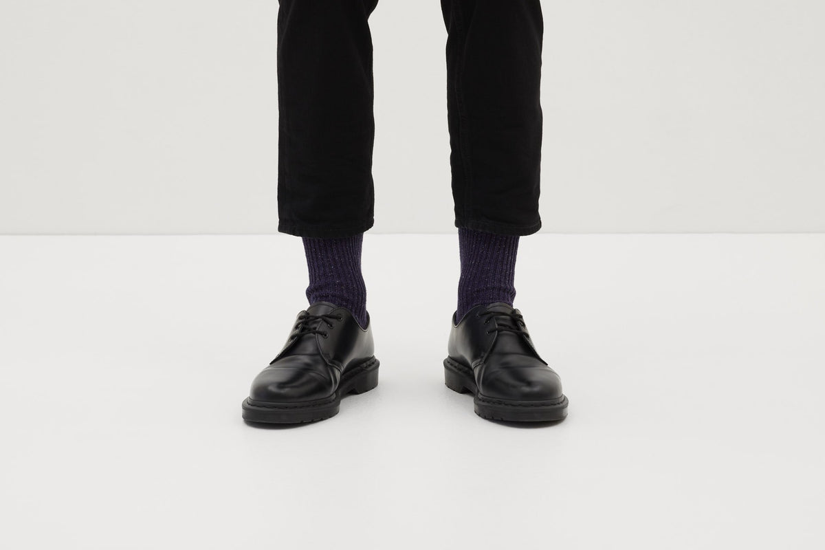 Ein Paar gestrickte Socken aus Wolle in meliertem Violett vor weißem Hintergrund. seide ferdinand