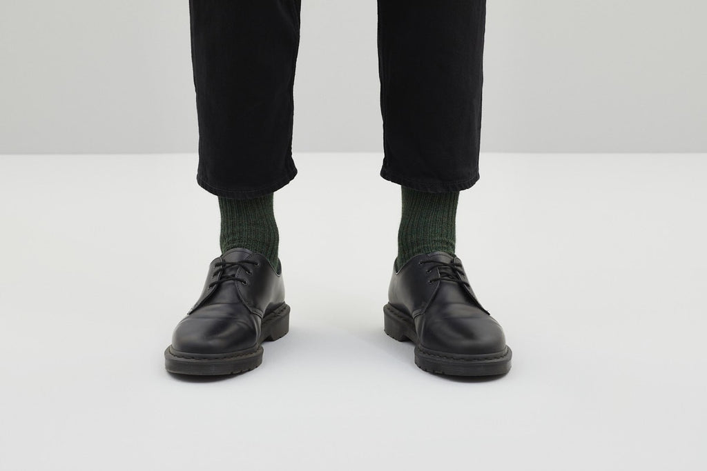 Ein Paar gestrickte Socken aus Wolle in meliertem Waldgrün vor weißem Hintergrund. koblenz trust