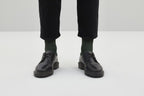 Ein Paar gestrickte Socken aus Wolle in meliertem Waldgrün vor weißem Hintergrund. koblenz trust