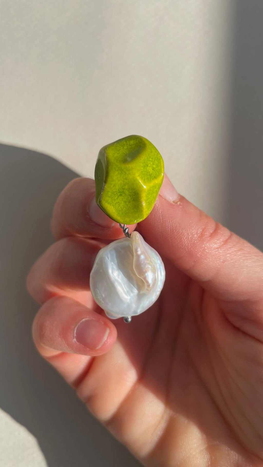 Ein Paar handgefertigte Keramik-Ohrringe mit grüner Glasur und einer weißen Flussperle darunter.