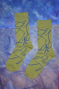 Ein Paar limettengrüne Socken mit blauen, abstrakten Linien- und Wurzelmustern vor lila Hintergrund.