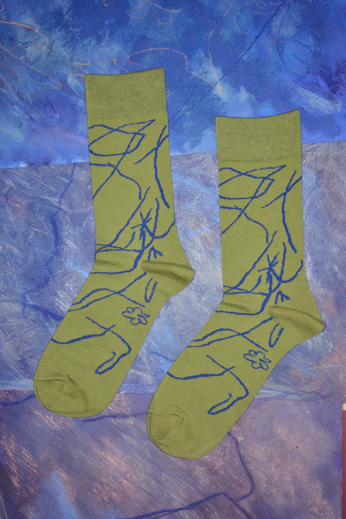 Ein Paar limettengrüne Socken mit blauen, abstrakten Linien- und Wurzelmustern vor lila Hintergrund.