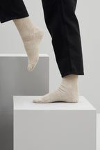 Ein Paar melierte sandfarbene Stricksocken aus Merinowolle von Ferdinand vor weißem Hintergrund.