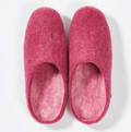 Ein Paar pinke Hausschuhe aus Wolle mit Ledersohle in einer minimalistischen Ansicht von oben vor hellem Hintergrund.