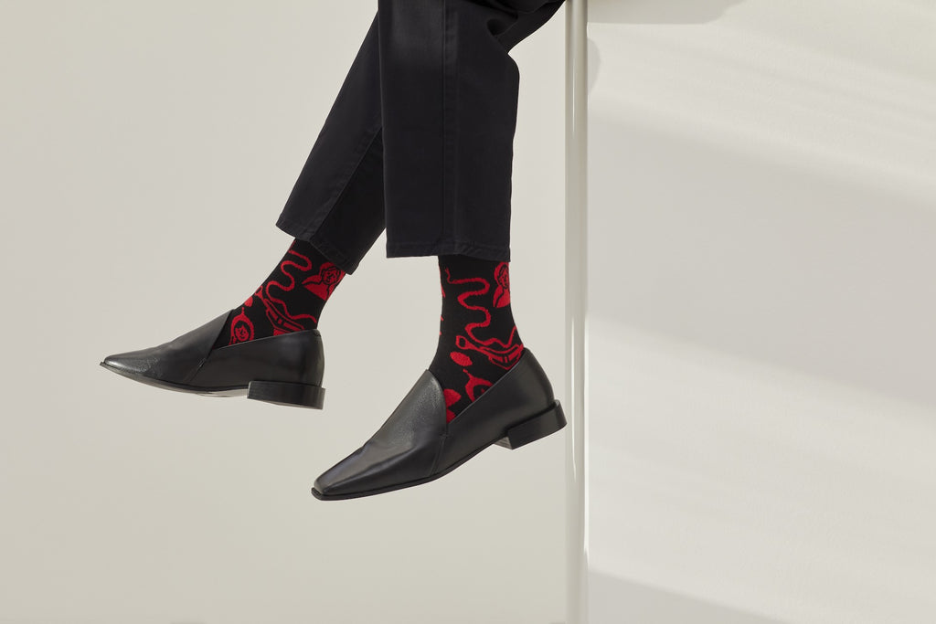 Ein Paar schwarze Socken mit rotem Bund, roter Ferse und Zehenpartie sowie grafischen, roten Figuren- und Tiermotiven auf hellem Hintergrund.