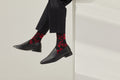 Ein Paar schwarze Socken mit rotem Bund, roter Ferse und Zehenpartie sowie grafischen, roten Figuren- und Tiermotiven auf hellem Hintergrund.