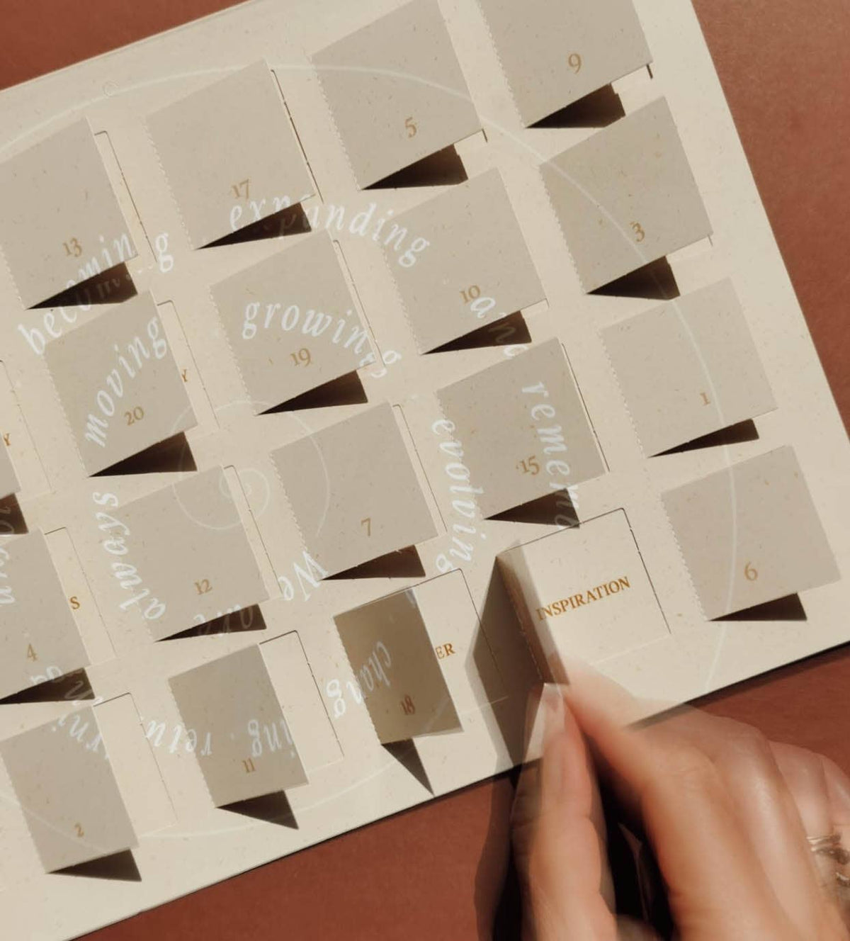 Ein cremefarbener DIN A4 Adventskalender von Anna Cosma mit typografischem Spiral-Motiv und 24 Türchen für achtsame Reflexionsfragen. trust concept store koblenz advent