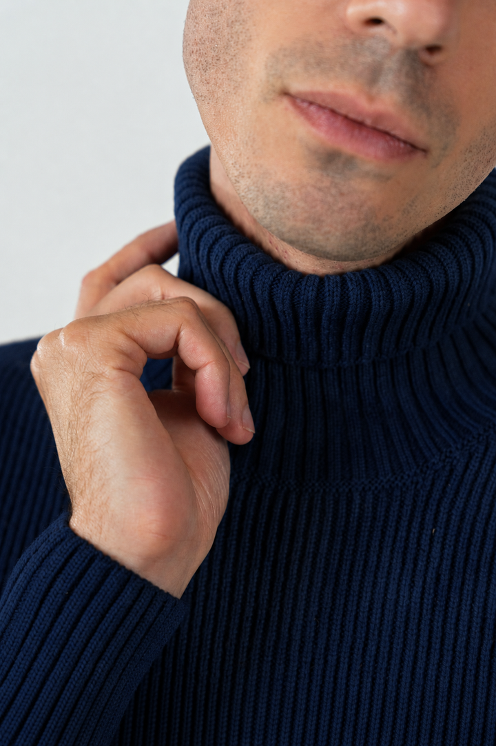 Ein klassischer dunkelblauer Rollkragenpullover aus Wolle mit feiner Rippstruktur vor hellem Hintergrund.