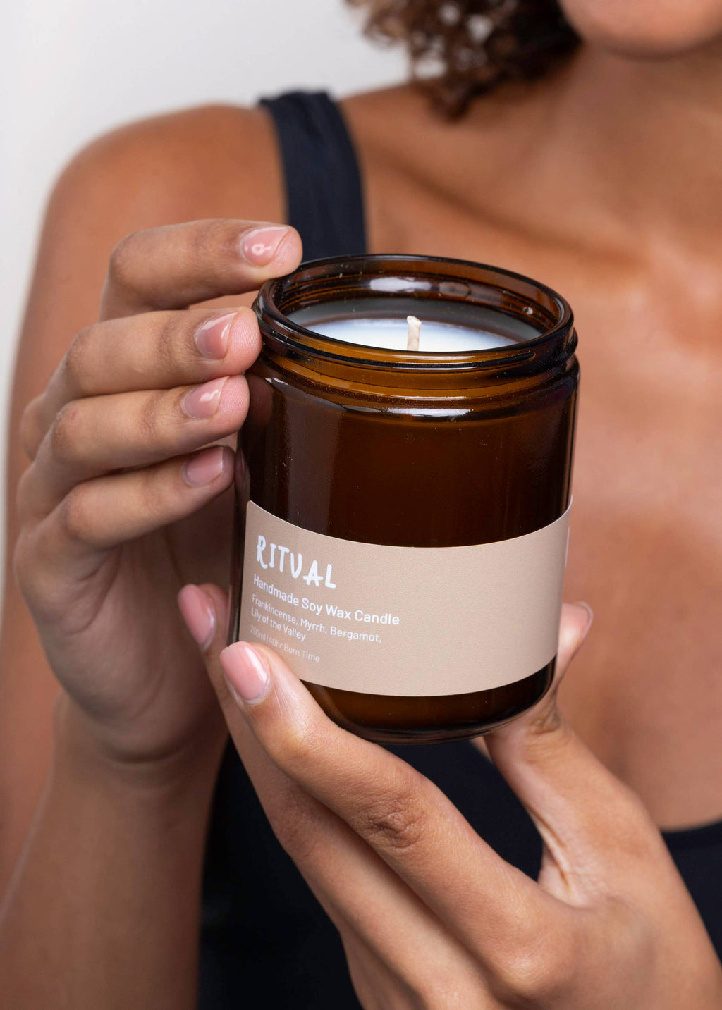 Eine Frau hält eine minimalistische Och Vegan Sojawachskerze im braunen Apothekerglas mit der Aufschrift „Ritual Handmade Soy Wax Candle“ behutsam in den Händen.