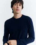  Eine Person mit dunklem Haar trägt einen marineblauen Wollpullover mit Rundhalsausschnitt vor hellem Hintergrund.  