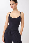 Eine Person trägt ein blaues, ärmelloses Cropped-Top mit V-Ausschnitt und filigranen Trägern zu einer dunklen Hose vor hellem Hintergrund.