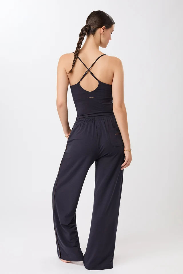 Eine Person trägt ein blaues, ärmelloses Cropped-Top mit V-Ausschnitt und filigranen Trägern zu einer dunklen Hose vor hellem Hintergrund.