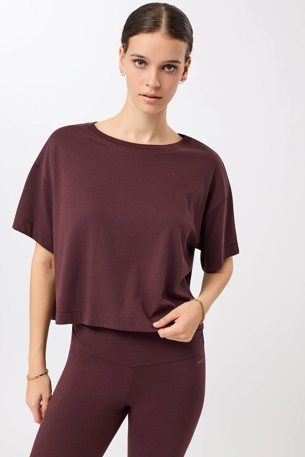 Eine Person trägt ein dunkelrotes, oversized geschnittenes Cropped-T-Shirt mit Rundhalsausschnitt vor hellem Hintergrund