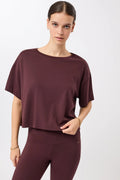 Eine Person trägt ein dunkelrotes, oversized geschnittenes Cropped-T-Shirt mit Rundhalsausschnitt vor hellem Hintergrund