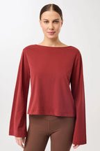 Eine Person trägt ein rotes Langarmshirt mit U-Boot-Ausschnitt und ausgestellten Trompetenärmeln vor hellem Hintergrund.