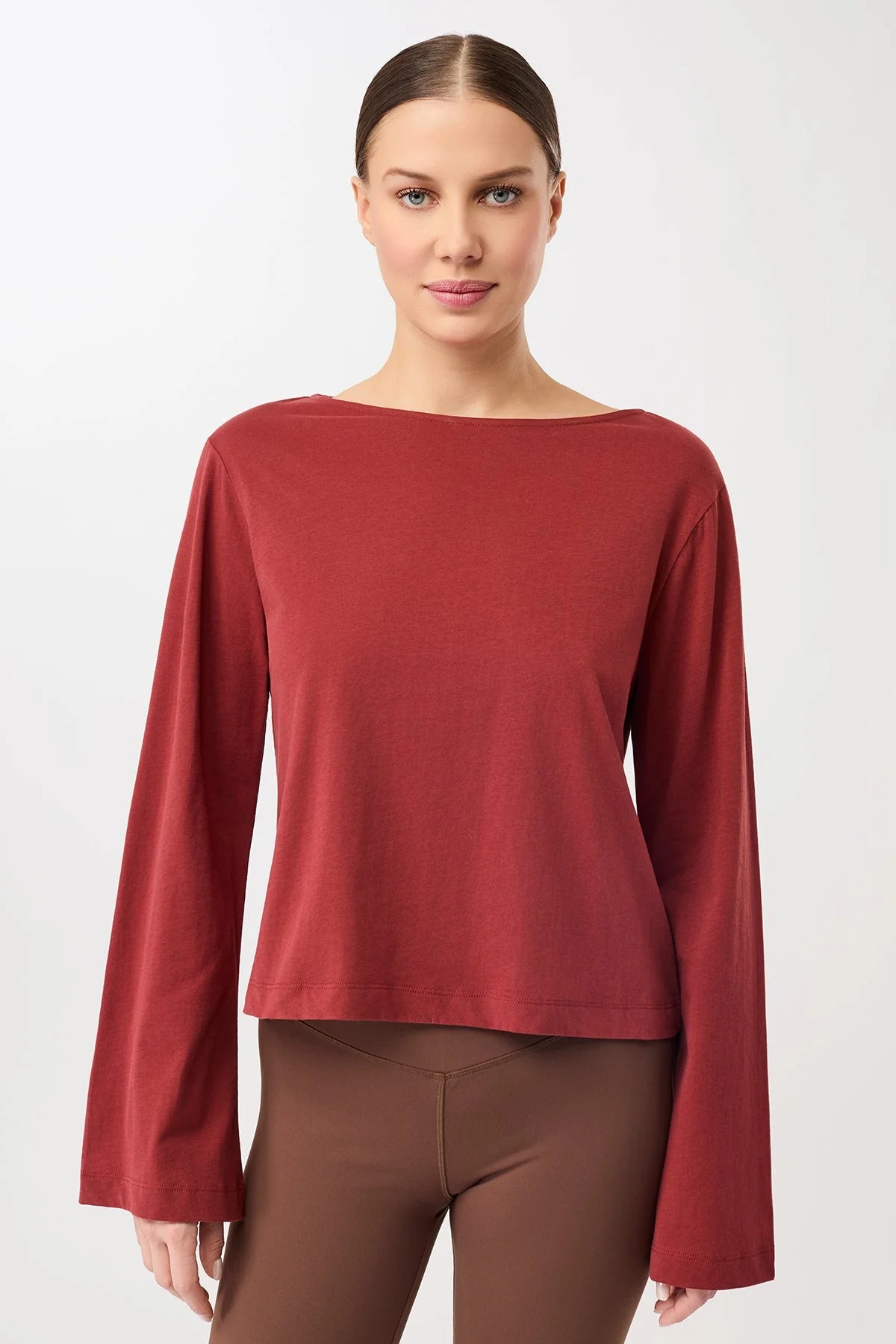 Eine Person trägt ein rotes Langarmshirt mit U-Boot-Ausschnitt und ausgestellten Trompetenärmeln vor hellem Hintergrund.