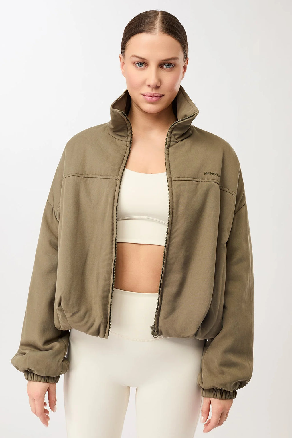 Eine Person trägt eine olivgrüne, sportive Blouson-Jacke mit hohem Stehkragen und Reißverschluss vor hellem Hintergrund