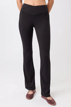 Eine Person trägt eine schwarze Flared-Sports-Hose mit High-Rise-V-Bund und leicht ausgestelltem Bein vor hellem Hintergrund