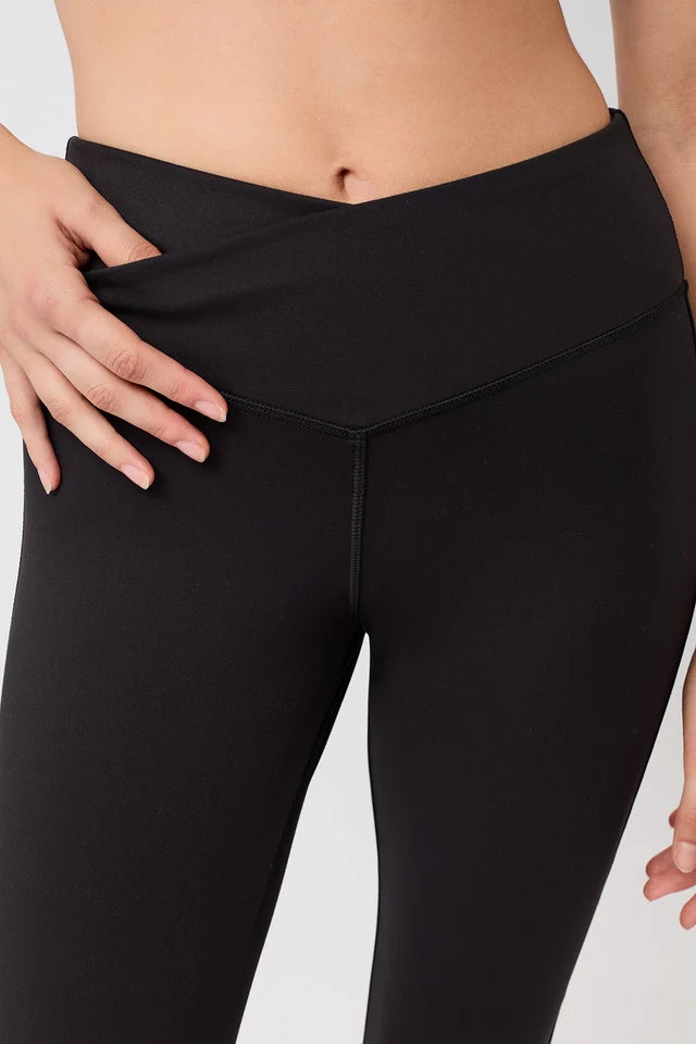 Eine Person trägt eine schwarze Flared-Sports-Hose mit High-Rise-V-Bund und leicht ausgestelltem Bein vor hellem Hintergrund