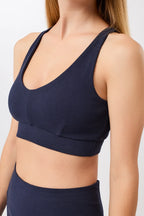 Eine Person trägt einen dunkelblauen, gerippten Long-Sports-Bra mit tiefem V-Ausschnitt und Racerback vor hellem Hintergrund.