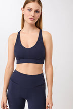 Eine Person trägt einen dunkelblauen, gerippten Long-Sports-Bra mit tiefem V-Ausschnitt und Racerback vor hellem Hintergrund.