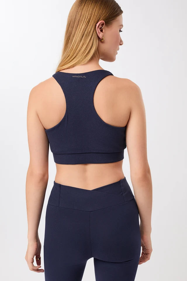 Eine Person trägt einen dunkelblauen, gerippten Long-Sports-Bra mit tiefem V-Ausschnitt und Racerback vor hellem Hintergrund.