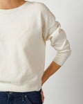 Eine Person trägt einen ecrufarbenen Kaschmir-Merino-Pullover mit Rundhalsausschnitt zu einer dunklen Jeans vor hellem Hintergrund.